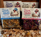 Four bags of Lil' Deuce Coop dried herbs and flowers arranged on wood with shavings. The packages are Diva Fresh, Diva Boost, Diva Dust, and Diva Nest, each showing illustrated hens and different dried botanical contents in clear bags with white labels and colored borders.